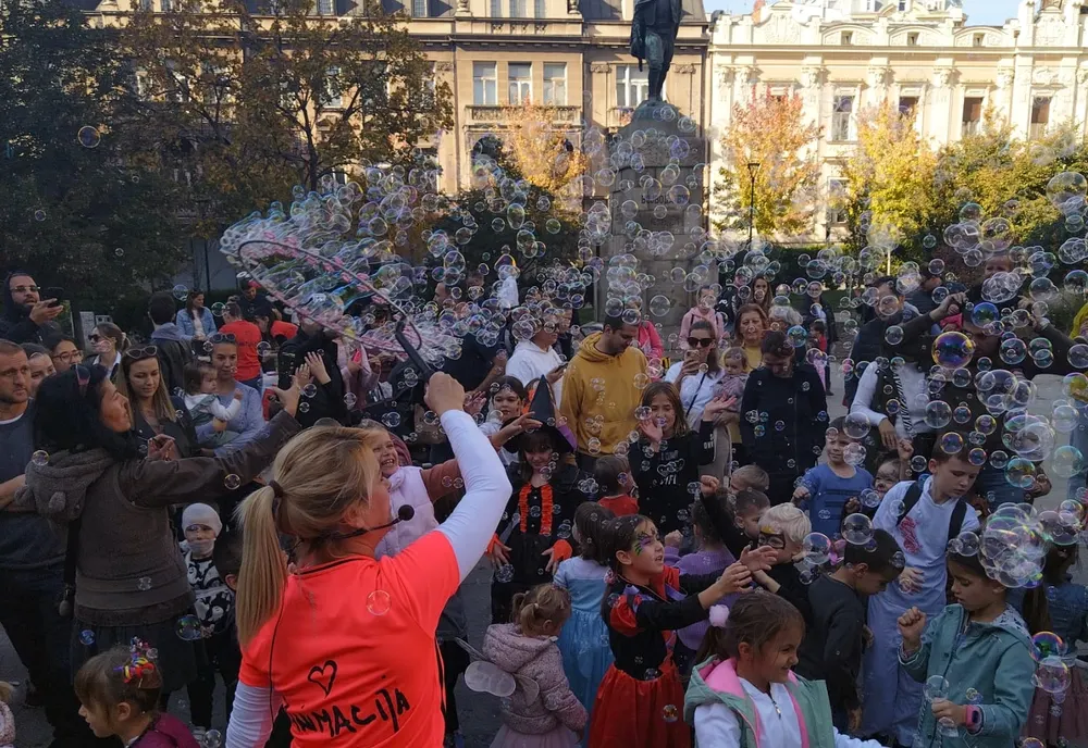 Animatorka vodi igru sa gomilom dece na gradskom trgu